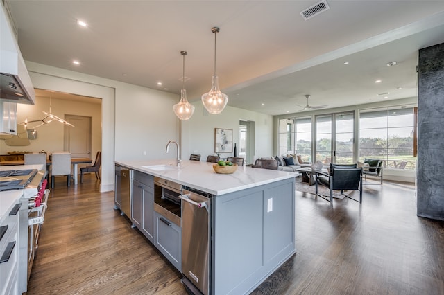 kitchen featuring pendant lighting, dark wood-type flooring, an island with sink, custom range hood, and appliances with stainless steel finishes