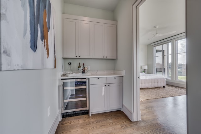 bar with ceiling fan, light hardwood / wood-style flooring, wine cooler, and white cabinets