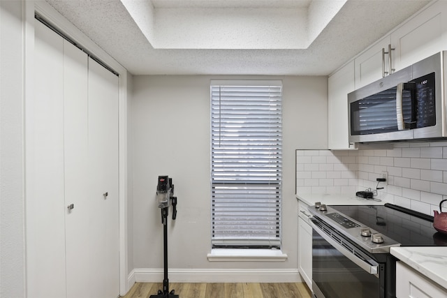 kitchen with white cabinets, appliances with stainless steel finishes, tasteful backsplash, and light hardwood / wood-style flooring