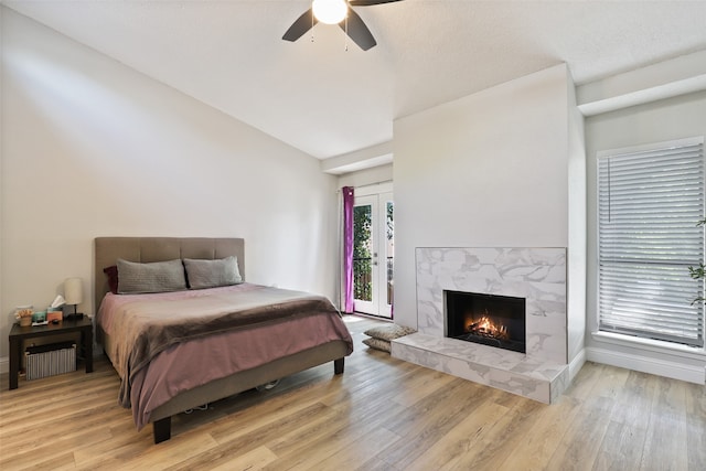 bedroom with ceiling fan, lofted ceiling, a high end fireplace, light wood-type flooring, and access to exterior