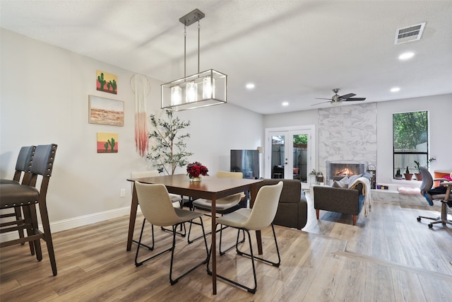 dining area with ceiling fan with notable chandelier, wood-type flooring, a fireplace, and french doors