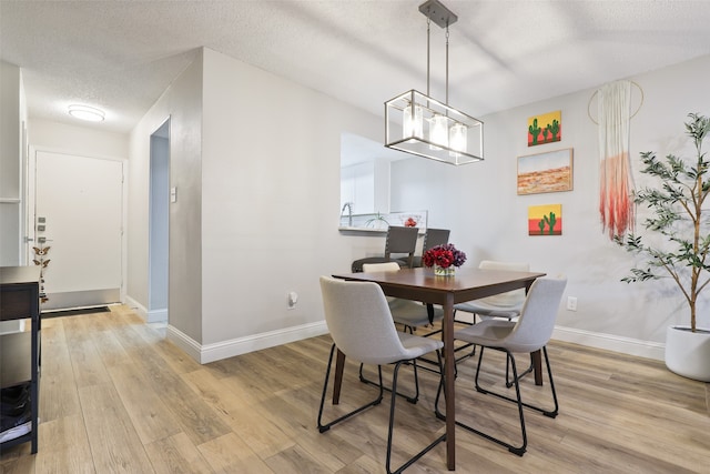 dining space featuring light wood-type flooring, a textured ceiling, and an inviting chandelier