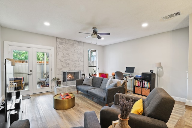 living room featuring a tiled fireplace, ceiling fan, light hardwood / wood-style floors, and french doors