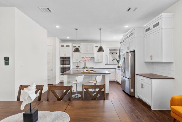 kitchen with a center island, appliances with stainless steel finishes, white cabinetry, dark wood-type flooring, and pendant lighting