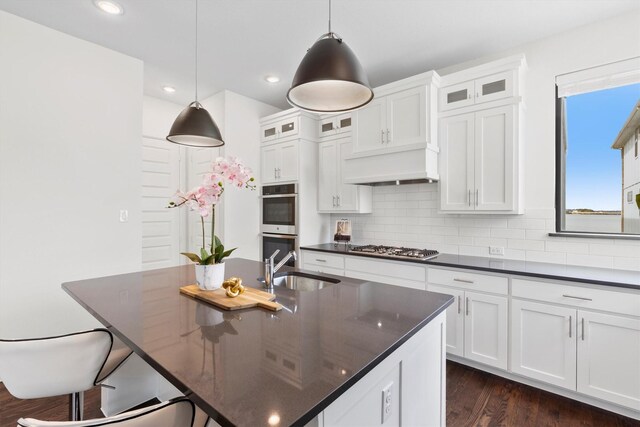 kitchen featuring decorative light fixtures, white cabinets, dark hardwood / wood-style flooring, and a kitchen island with sink