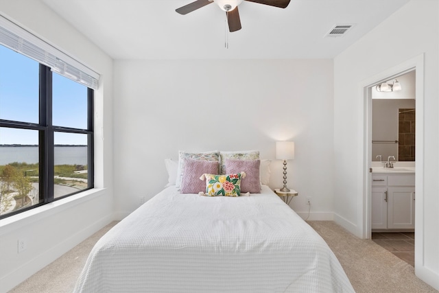 bedroom with light colored carpet, ensuite bath, multiple windows, and ceiling fan