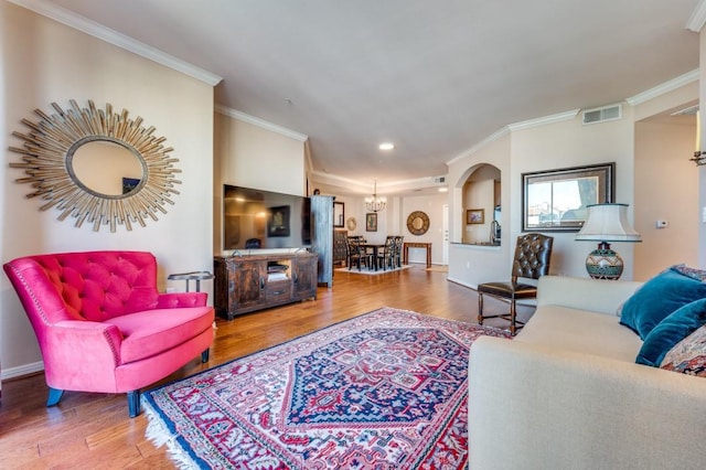 living area with visible vents, wood finished floors, an inviting chandelier, and ornamental molding