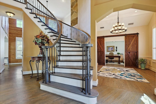 foyer entrance featuring hardwood / wood-style floors, wooden walls, a notable chandelier, and a towering ceiling