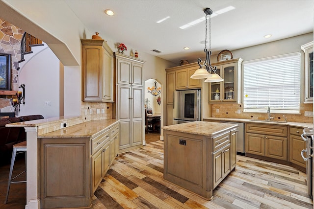 kitchen featuring light hardwood / wood-style flooring, appliances with stainless steel finishes, sink, kitchen peninsula, and a kitchen island