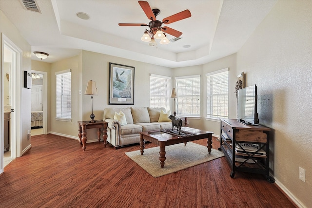 living room with a tray ceiling, dark wood-type flooring, and ceiling fan