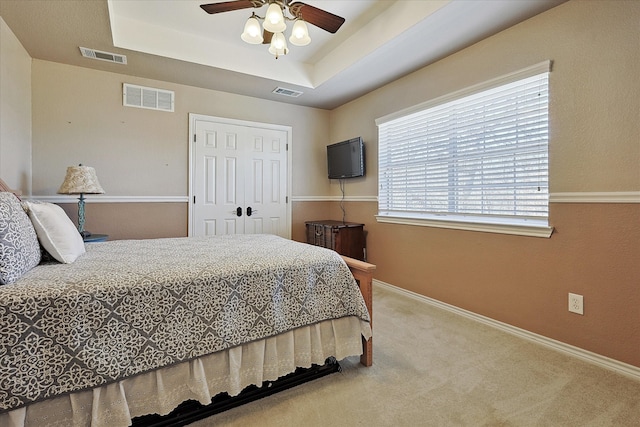 carpeted bedroom featuring a raised ceiling, ceiling fan, and a closet