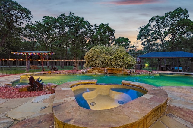 pool at dusk with an in ground hot tub, a gazebo, and a patio