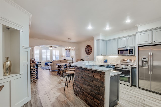 kitchen featuring appliances with stainless steel finishes, light stone counters, light hardwood / wood-style floors, kitchen peninsula, and ornamental molding