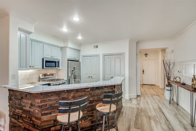 kitchen featuring ornamental molding, kitchen peninsula, decorative backsplash, appliances with stainless steel finishes, and light hardwood / wood-style floors