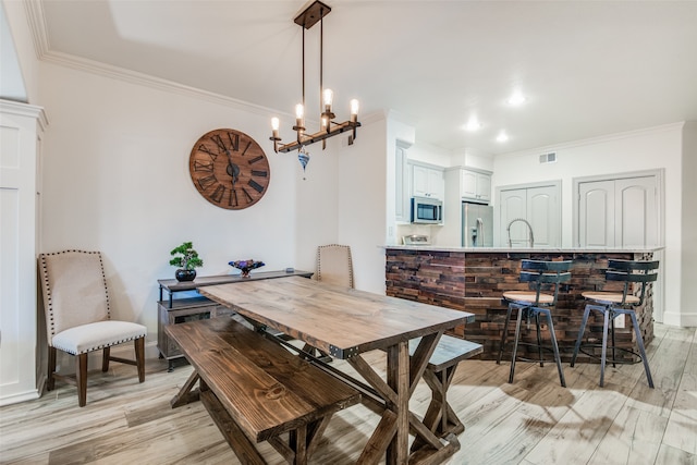 dining area with crown molding, an inviting chandelier, sink, and light hardwood / wood-style floors