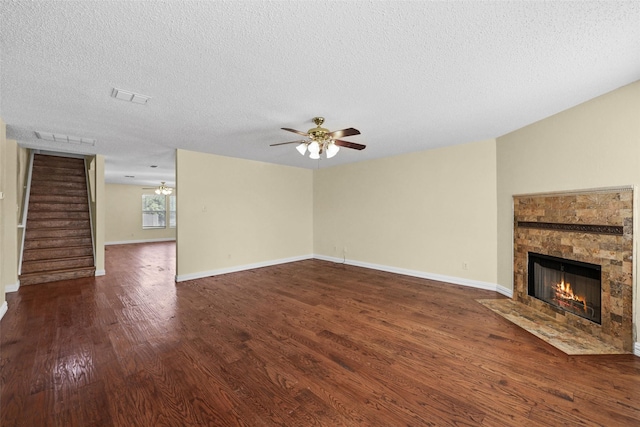 unfurnished living room with a stone fireplace, dark hardwood / wood-style floors, a textured ceiling, and ceiling fan