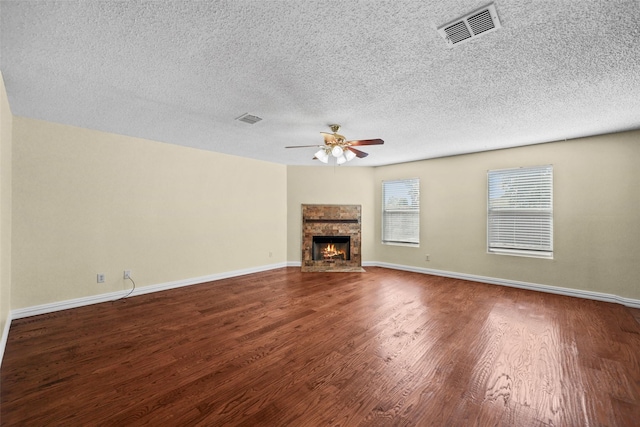 unfurnished living room featuring ceiling fan, a fireplace, dark hardwood / wood-style floors, and a textured ceiling