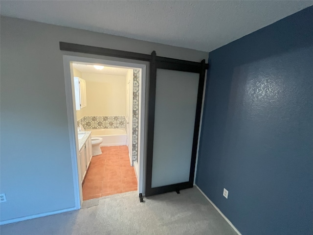 unfurnished bedroom featuring carpet floors, ensuite bathroom, a barn door, and a textured ceiling