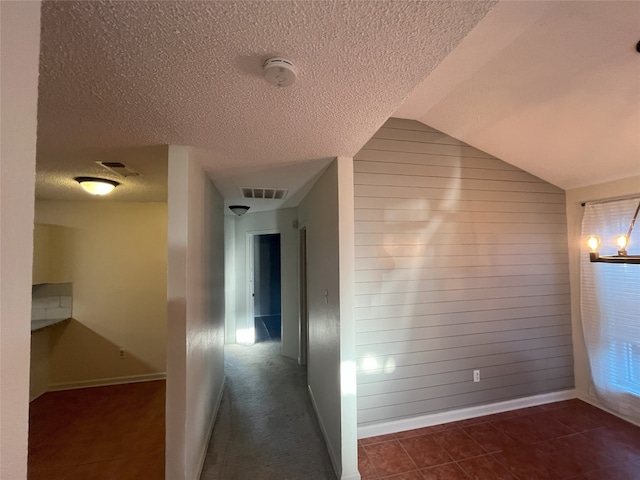 hallway featuring dark tile patterned flooring, a textured ceiling, vaulted ceiling, an inviting chandelier, and wooden walls