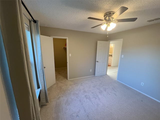 unfurnished bedroom with ceiling fan, a textured ceiling, a closet, a spacious closet, and light carpet