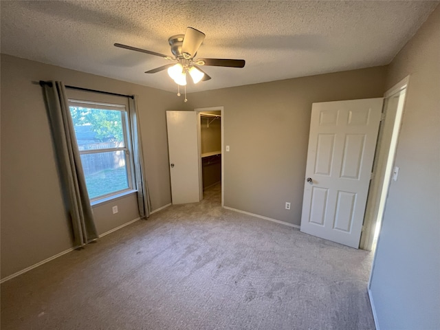 unfurnished bedroom with a spacious closet, a closet, a textured ceiling, ceiling fan, and light carpet