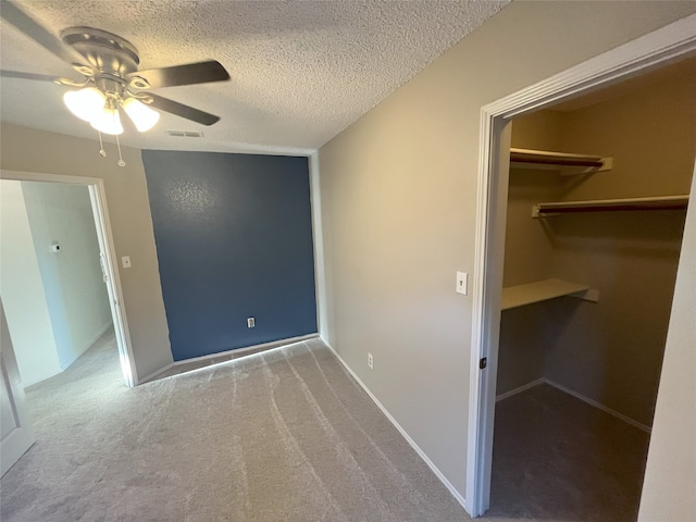 unfurnished bedroom with a closet, a textured ceiling, carpet flooring, a spacious closet, and ceiling fan