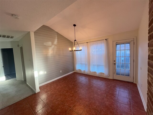 unfurnished dining area featuring lofted ceiling, dark tile patterned floors, a textured ceiling, wooden walls, and an inviting chandelier