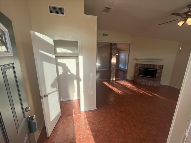 unfurnished living room featuring ceiling fan, dark tile patterned floors, and a brick fireplace