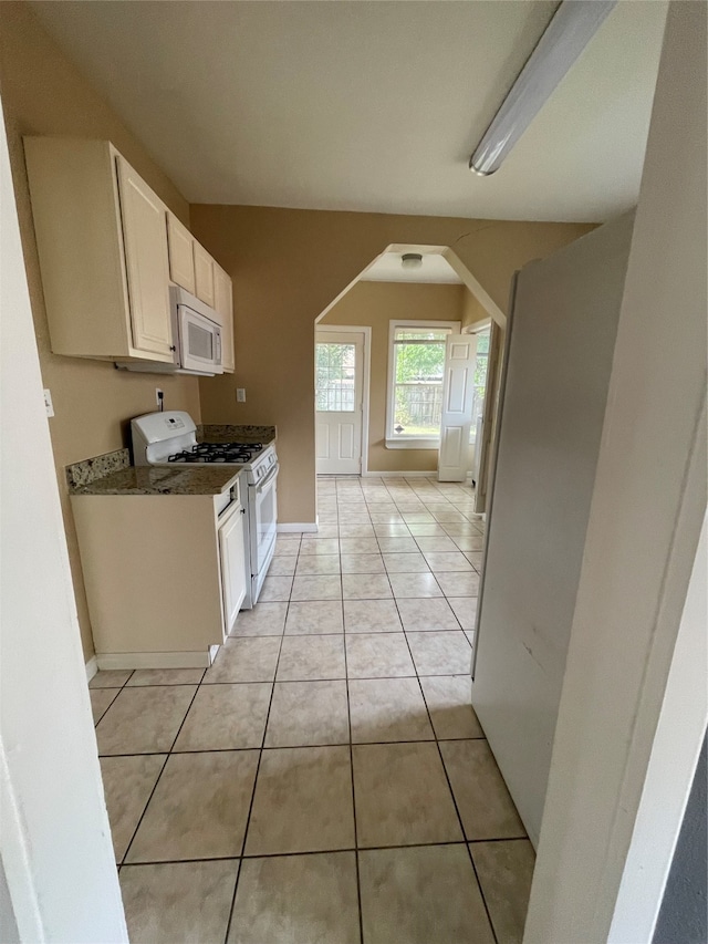 kitchen with white cabinets, white appliances, dark stone countertops, and light tile patterned flooring