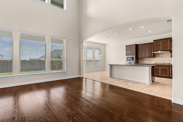 kitchen with arched walkways, dark brown cabinetry, appliances with stainless steel finishes, light wood finished floors, and decorative backsplash