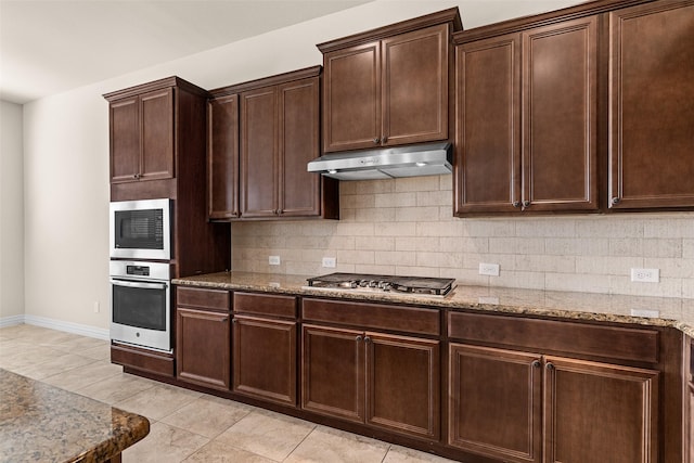 kitchen featuring under cabinet range hood, backsplash, appliances with stainless steel finishes, light tile patterned floors, and light stone countertops