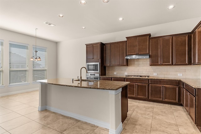 kitchen featuring dark stone countertops, visible vents, a center island with sink, appliances with stainless steel finishes, and backsplash