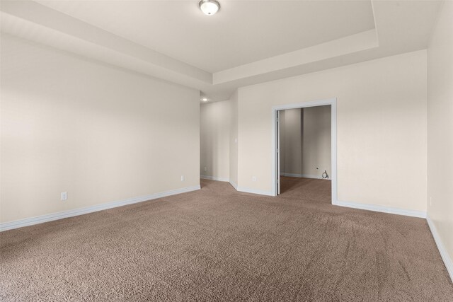 empty room featuring baseboards, a raised ceiling, and light carpet