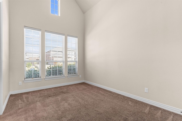 carpeted empty room featuring baseboards and high vaulted ceiling