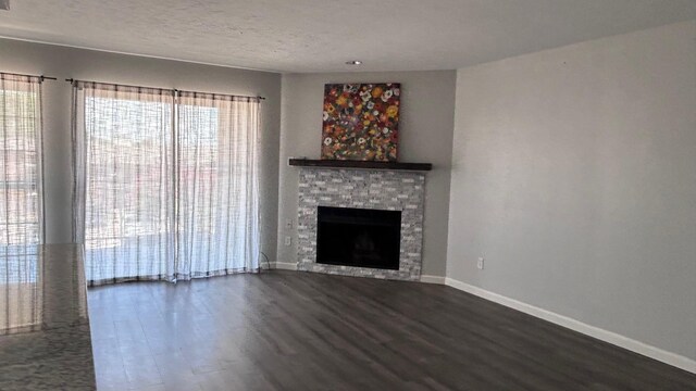 unfurnished living room featuring dark wood-type flooring, a textured ceiling, and a stone fireplace