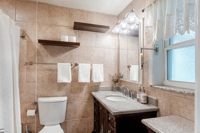 bathroom with a textured ceiling, vanity, toilet, and tile walls