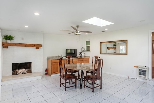 tiled dining room featuring a fireplace, a skylight, heating unit, and ceiling fan