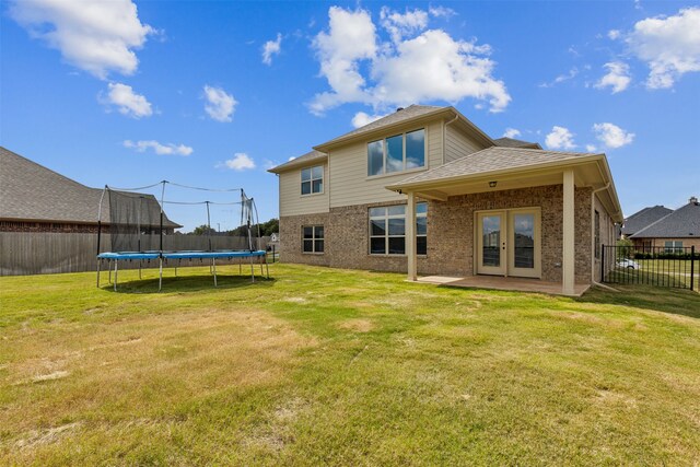 back of property with a yard, a patio area, and a trampoline