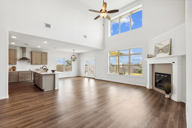 unfurnished living room with ceiling fan with notable chandelier, dark hardwood / wood-style flooring, sink, a brick fireplace, and a high ceiling