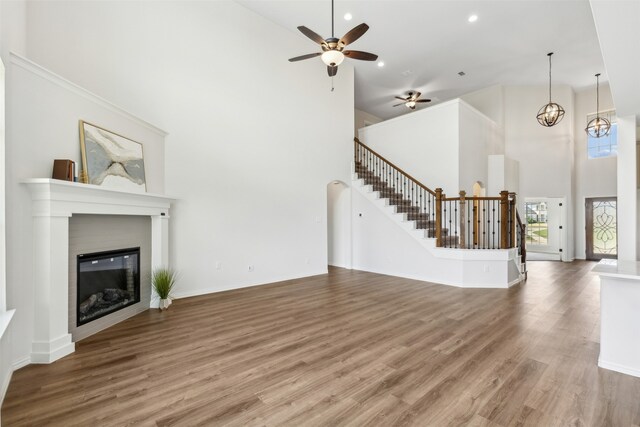 unfurnished living room featuring ceiling fan, a towering ceiling, and hardwood / wood-style floors