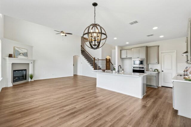 kitchen with wood-type flooring, an island with sink, hanging light fixtures, stainless steel appliances, and gray cabinets