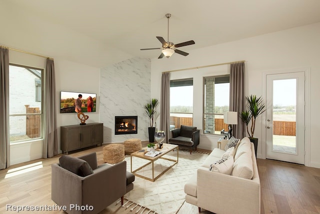 living room with ceiling fan, light wood-type flooring, vaulted ceiling, and a fireplace