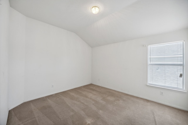 spare room featuring light carpet and vaulted ceiling