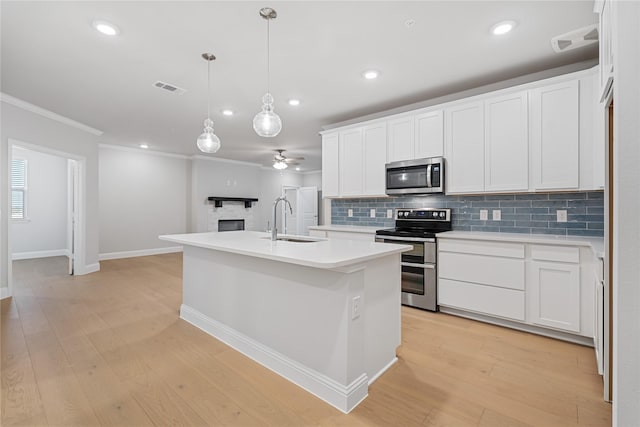 kitchen featuring sink, white cabinetry, decorative light fixtures, appliances with stainless steel finishes, and a kitchen island with sink