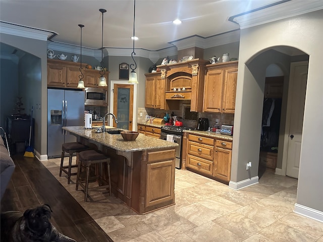 kitchen with light stone countertops, hanging light fixtures, an island with sink, appliances with stainless steel finishes, and sink