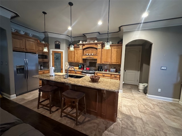 kitchen with appliances with stainless steel finishes, hanging light fixtures, an island with sink, light stone counters, and sink