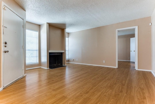 unfurnished living room featuring baseboards, light wood-style floors, a fireplace, and a textured ceiling