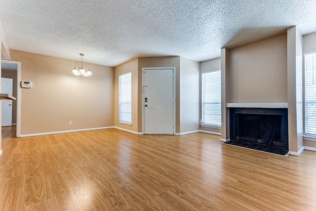 unfurnished living room featuring a notable chandelier, light wood-style flooring, a textured ceiling, baseboards, and a tile fireplace