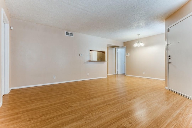 unfurnished living room with visible vents, baseboards, light wood-style floors, a notable chandelier, and a textured ceiling