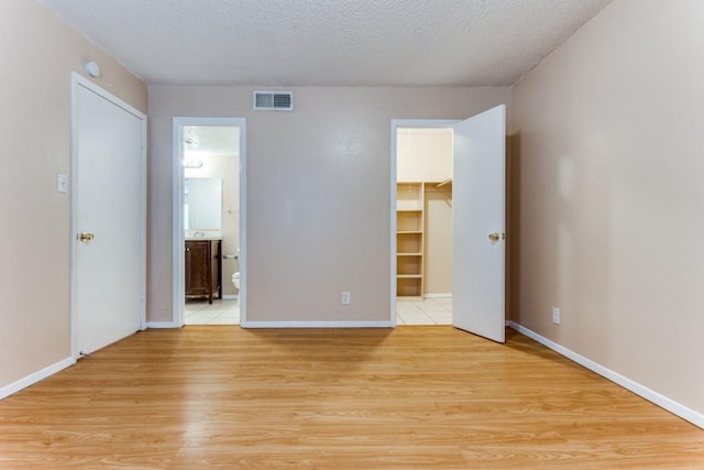 unfurnished bedroom featuring visible vents, light wood finished floors, ensuite bathroom, a textured ceiling, and a walk in closet